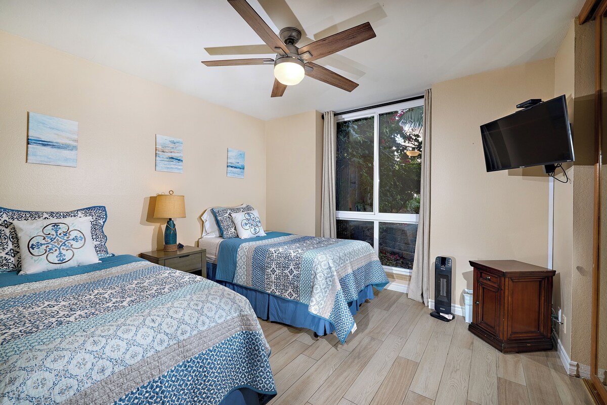 A bedroom with two beds, a ceiling fan, a TV, and a window.