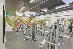 A gym with various exercise machines, a mirror wall, and a colorful geometric wall design. - Oceanside Beach Condos (Oceanside)