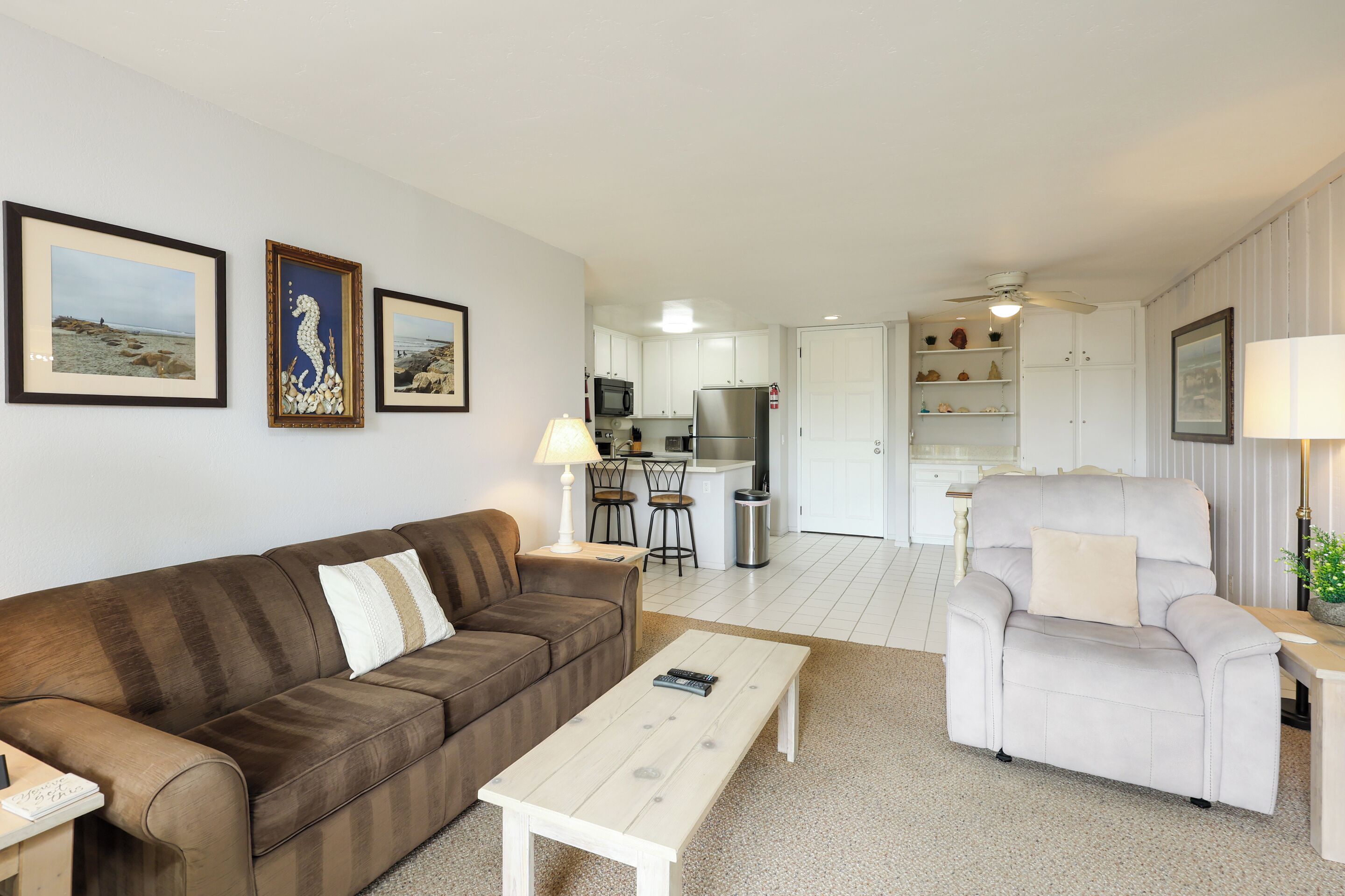 A living room with a brown sofa, a white armchair, a coffee table, and framed pictures on the wall.
