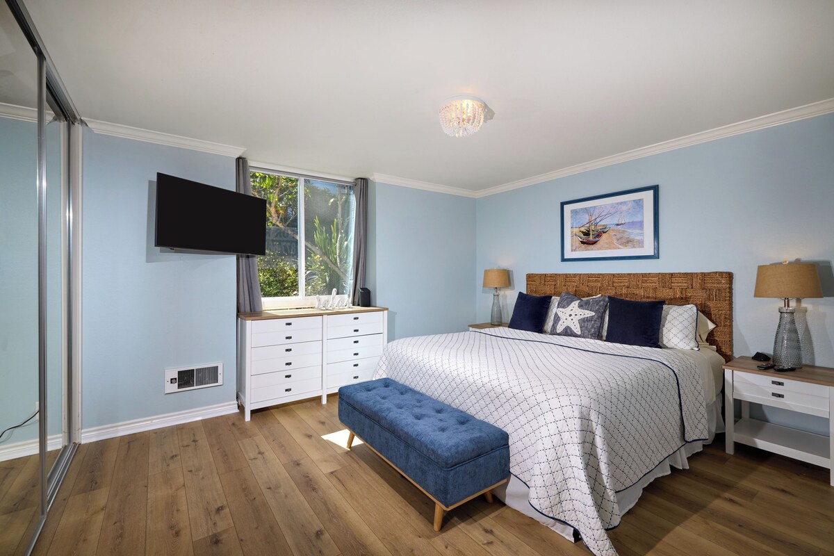 A bedroom with a bed, a flat-screen TV, a window, and a painting on the wall.