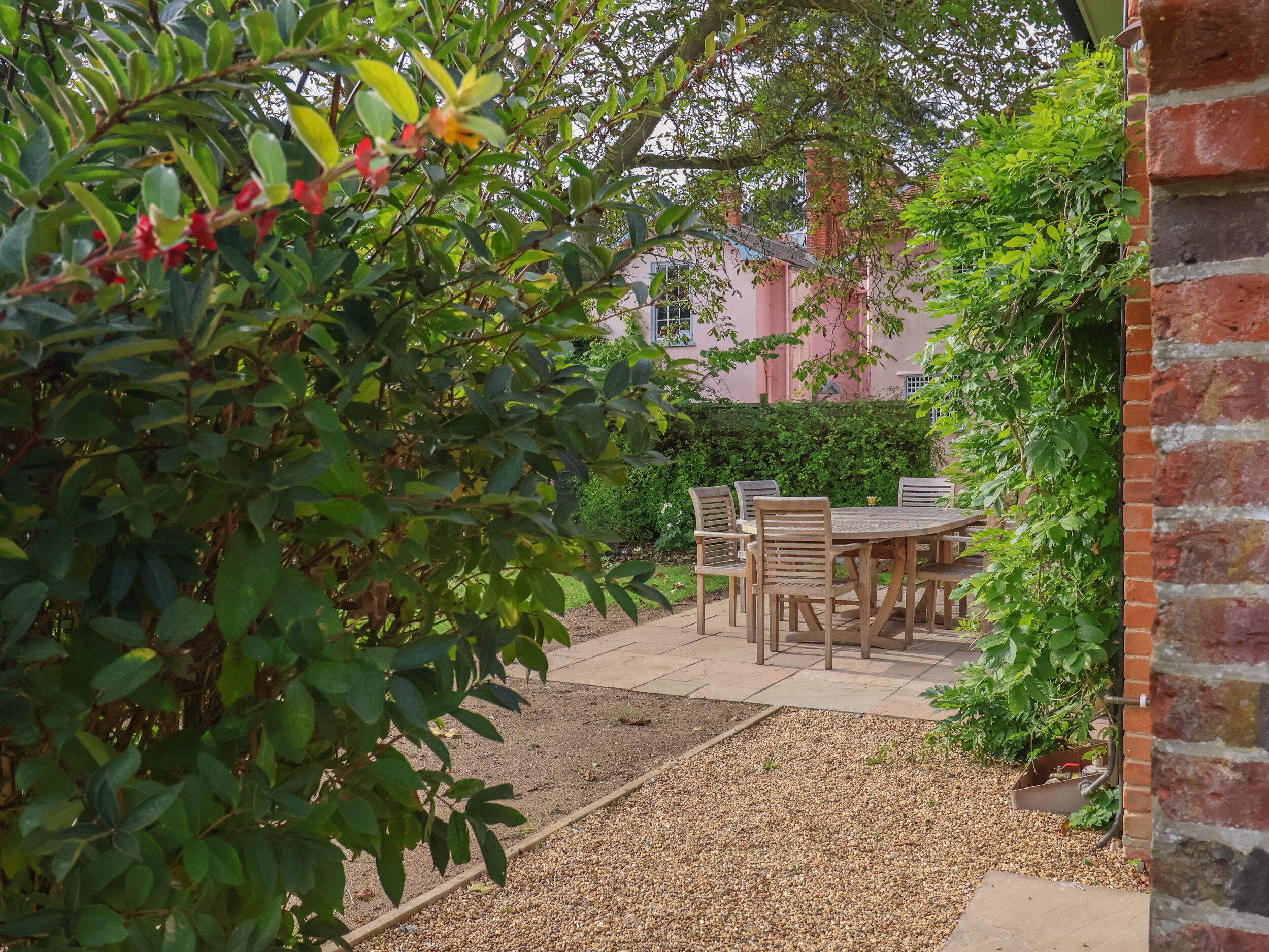 A patio with a wooden table and chairs, surrounded by greenery and a brick wall.