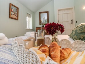 A neatly arranged breakfast table with croissants, a coffee pot, and a vase with flowers in a hotel room. - Rookery Cottage (Saxmundham)