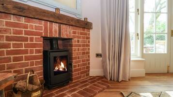 A brick fireplace with a modern wood-burning stove, a metal bucket with logs, and a wooden bench.