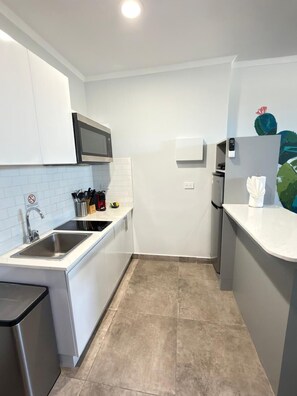 Una cocina compacta con armarios blancos, un lavamanos de acero inoxidable, un microondas y un refrigerador.