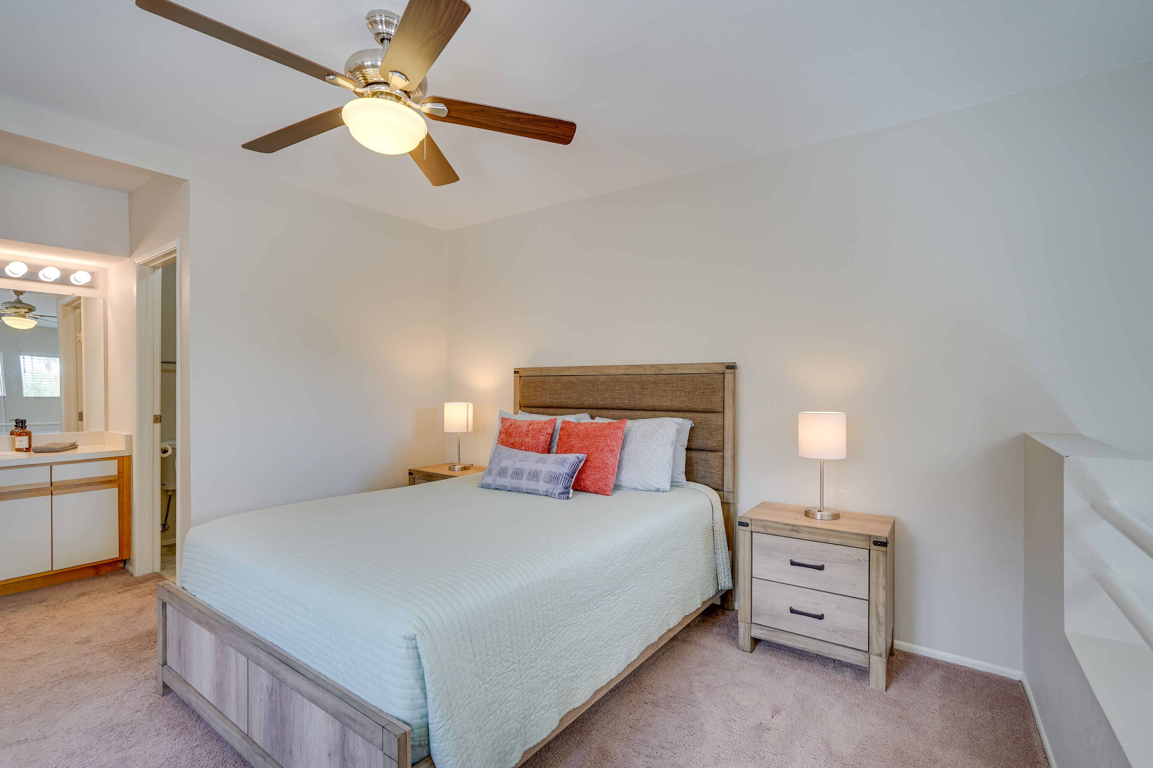 A bedroom with a bed, nightstands, a mirror, and a ceiling fan.