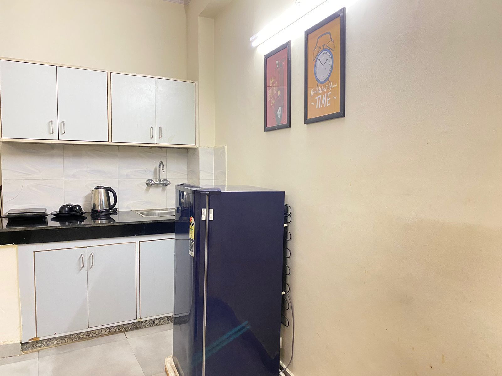 A small kitchenette with white cabinets, a sink, and a stove. There are two framed pictures on the wall.