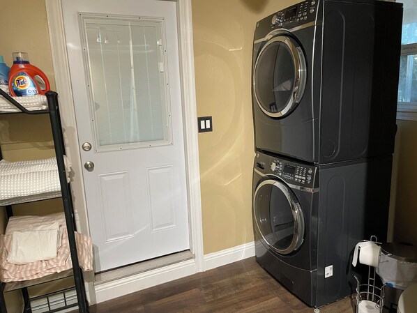 A laundry room with a front-loading washer and dryer, a door with a window, and a shelf with laundry supplies.