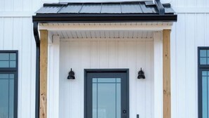 A white building with a black door, wooden columns, and a small porch with steps. - New Farmhouse-Hot Tub, King Beds, Game Room, Pro Golf Sim & Amazing Valley View! (Montgomery)