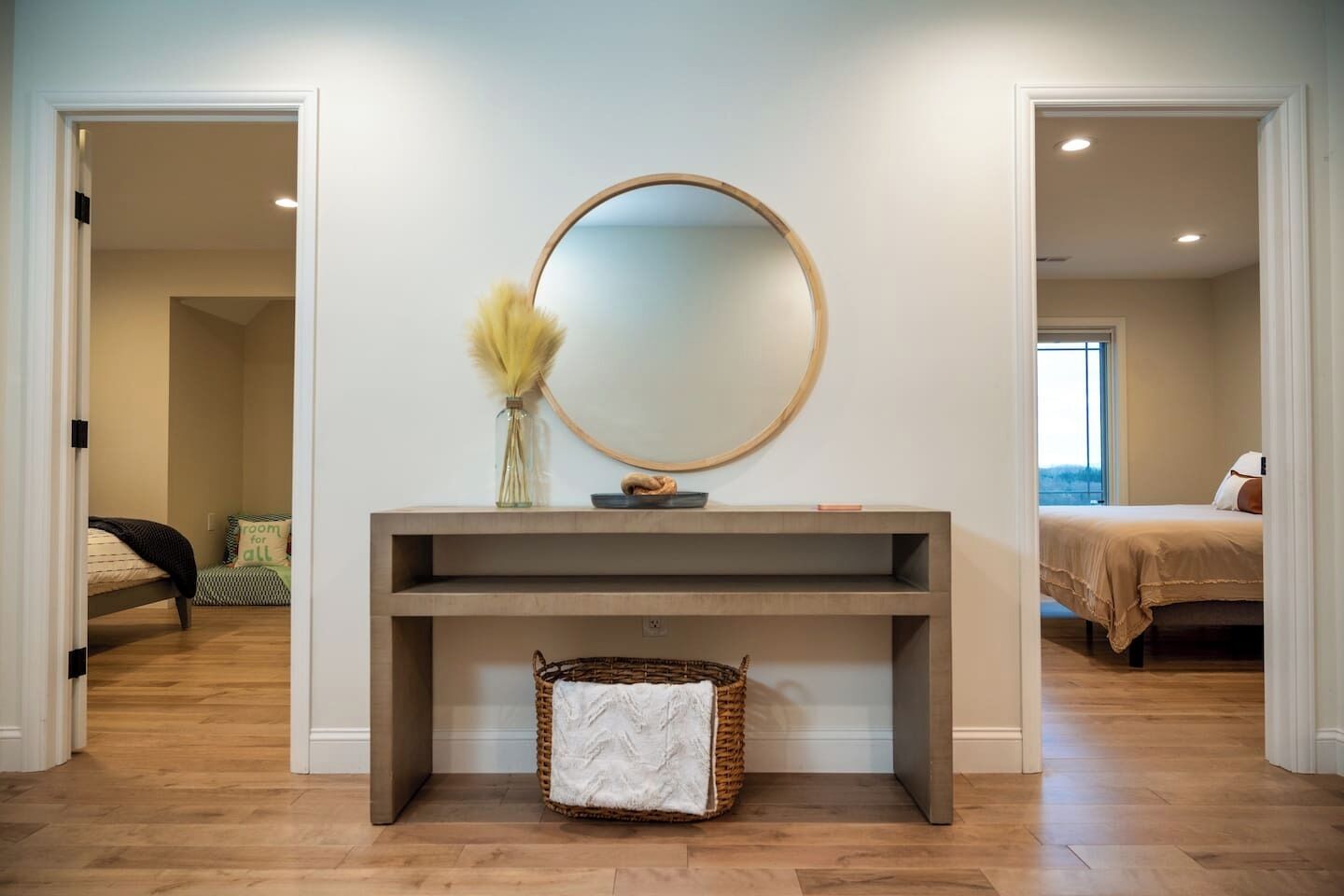 A modern bedroom with a large bed, a bedside table with a mirror, and a console table with a vase and basket.