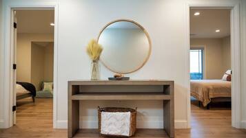 A modern bedroom with a large bed, a bedside table with a mirror, and a console table with a vase and basket.