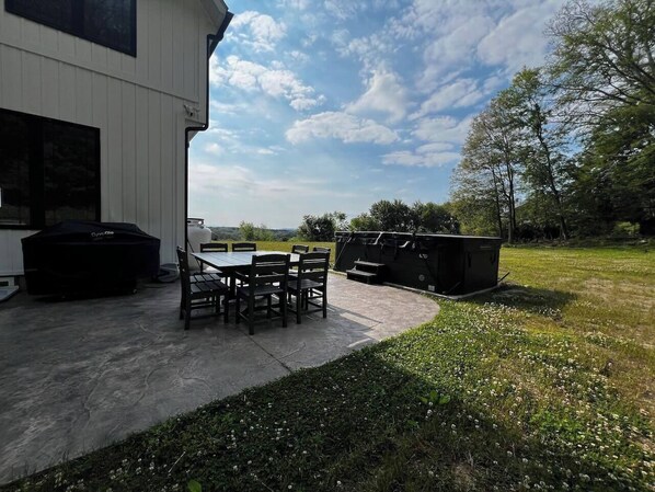 Un espace extérieur aménagé en terrasse, avec un sol en béton, une table et des chaises, ainsi qu’un barbecue.