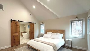 A bedroom with a large bed, wooden door, and a view of the outside through a window. - New Farmhouse-Hot Tub, King Beds, Game Room, Pro Golf Sim & Amazing Valley View! (Montgomery)