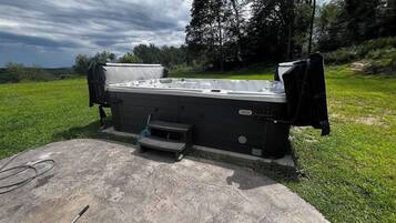 A hot tub with a cover, a small step stool, and a hose on a concrete surface in a grassy area.