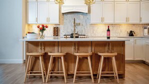A kitchen with white cabinets, a marble backsplash, and a central island with stools. - New Farmhouse-Hot Tub, King Beds, Game Room, Pro Golf Sim & Amazing Valley View! (Montgomery)