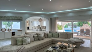 A modern living room with a large beige sectional sofa, a glass coffee table, and a view of a pool and outdoor seating area. - ★Luxury Villa Heated Pool, walk to São Rafael Beach, Albufeira (Albufeira)