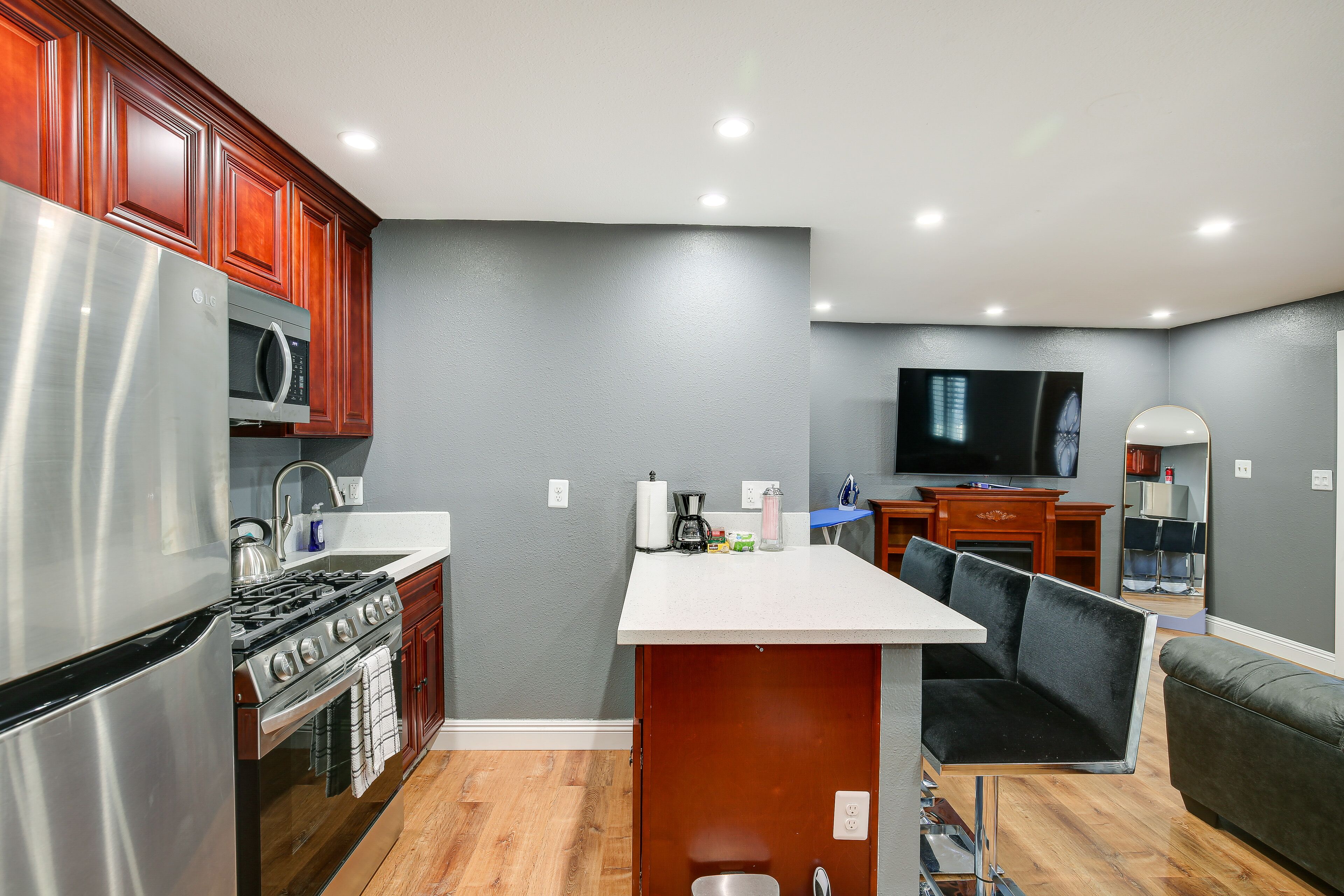 A compact kitchen with a refrigerator, microwave, stove, and sink. There is a dining area with a table and chairs, and a television in the background.