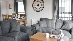 A modern living room with grey upholstered sofas, a wooden coffee table, and a wall clock. - Patrington Haven is a pristine lodge park with an array of facilities. (Patrington, near Hull)