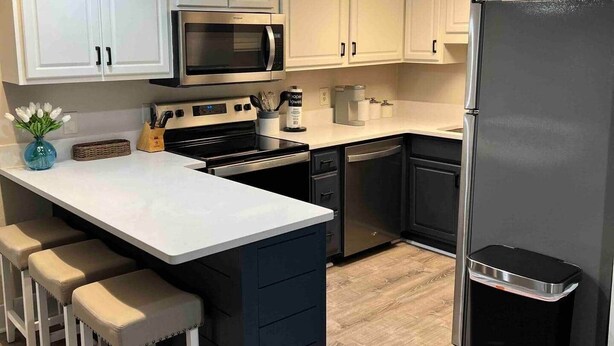 A modern kitchen with white cabinets, a black refrigerator, a microwave, a stove, and a bar area with stools.