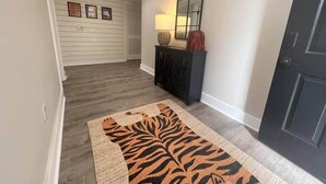 A hallway with a dark wood floor, a black door, a mirror, and a console table with decorative items.