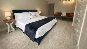 A bedroom with a bed, bedside tables, a sofa, and a wall-mounted light fixture.