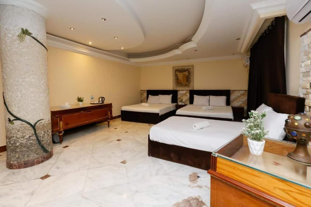 A hotel room with a large pillar, a bed, a bedside table, a dresser, and a painting on the wall.