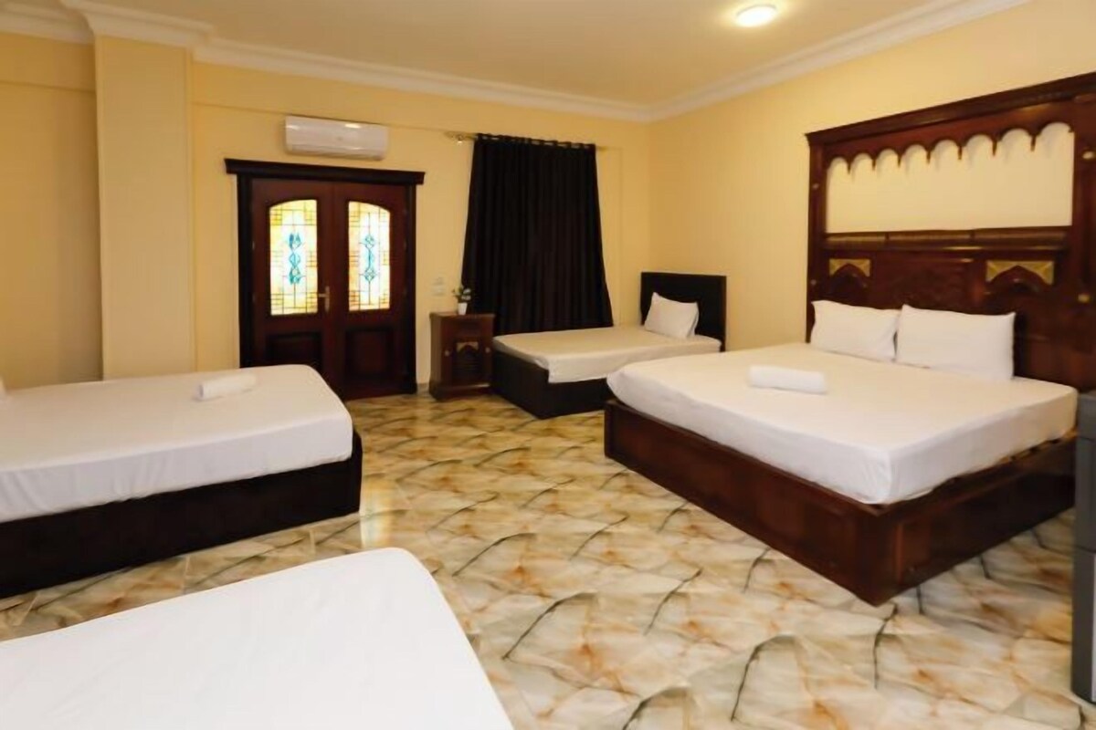 A hotel room with two single beds, a small table, and a window with curtains.