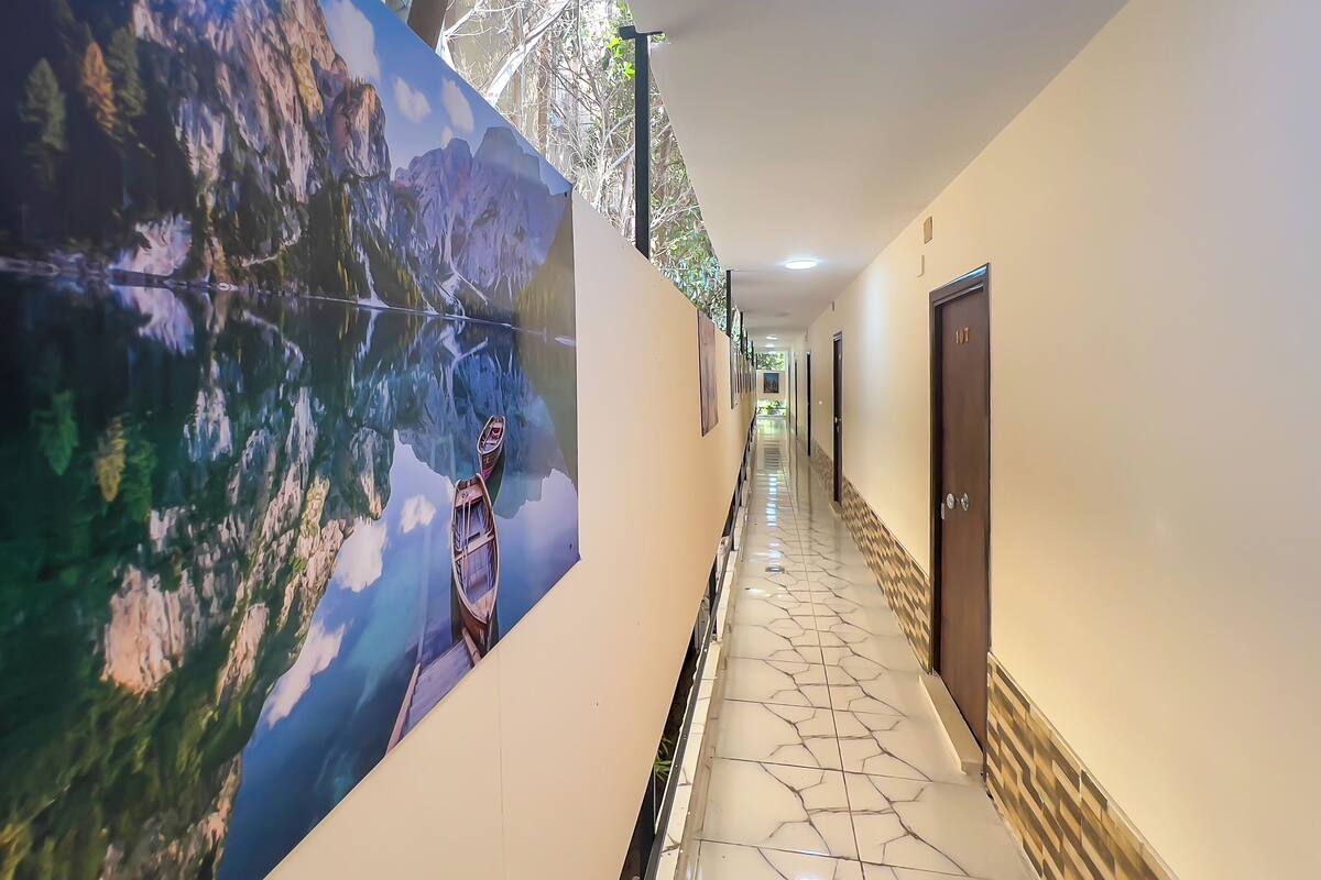 A hotel corridor with a large mural of a mountain landscape and a boat, tiled flooring, and doors on the right.