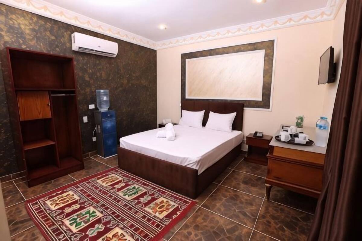 A hotel room with a bed, a wardrobe, a water dispenser, a desk, and a TV.