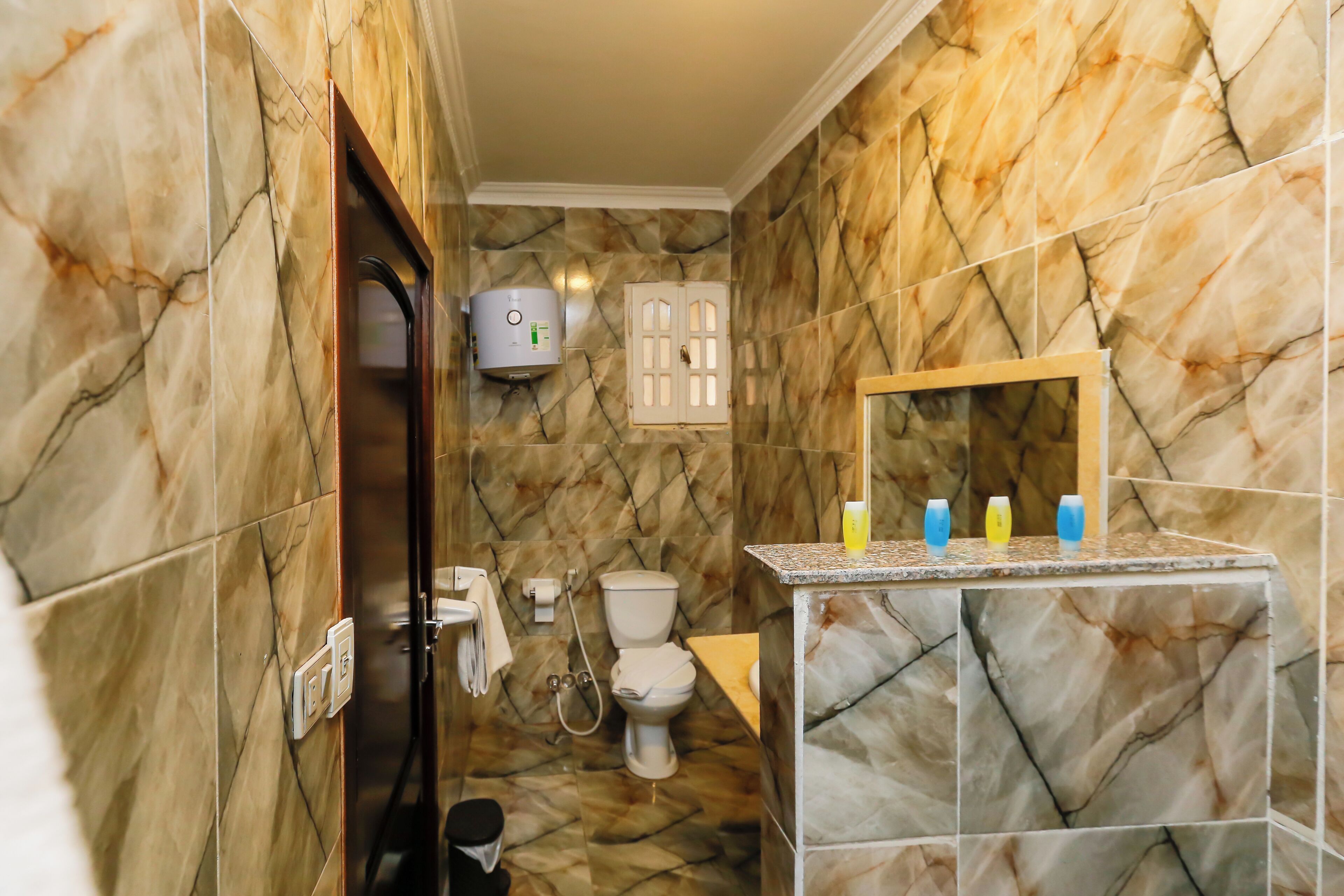 A bathroom with marble walls, a toilet, a sink with a mirror, and a hand dryer.