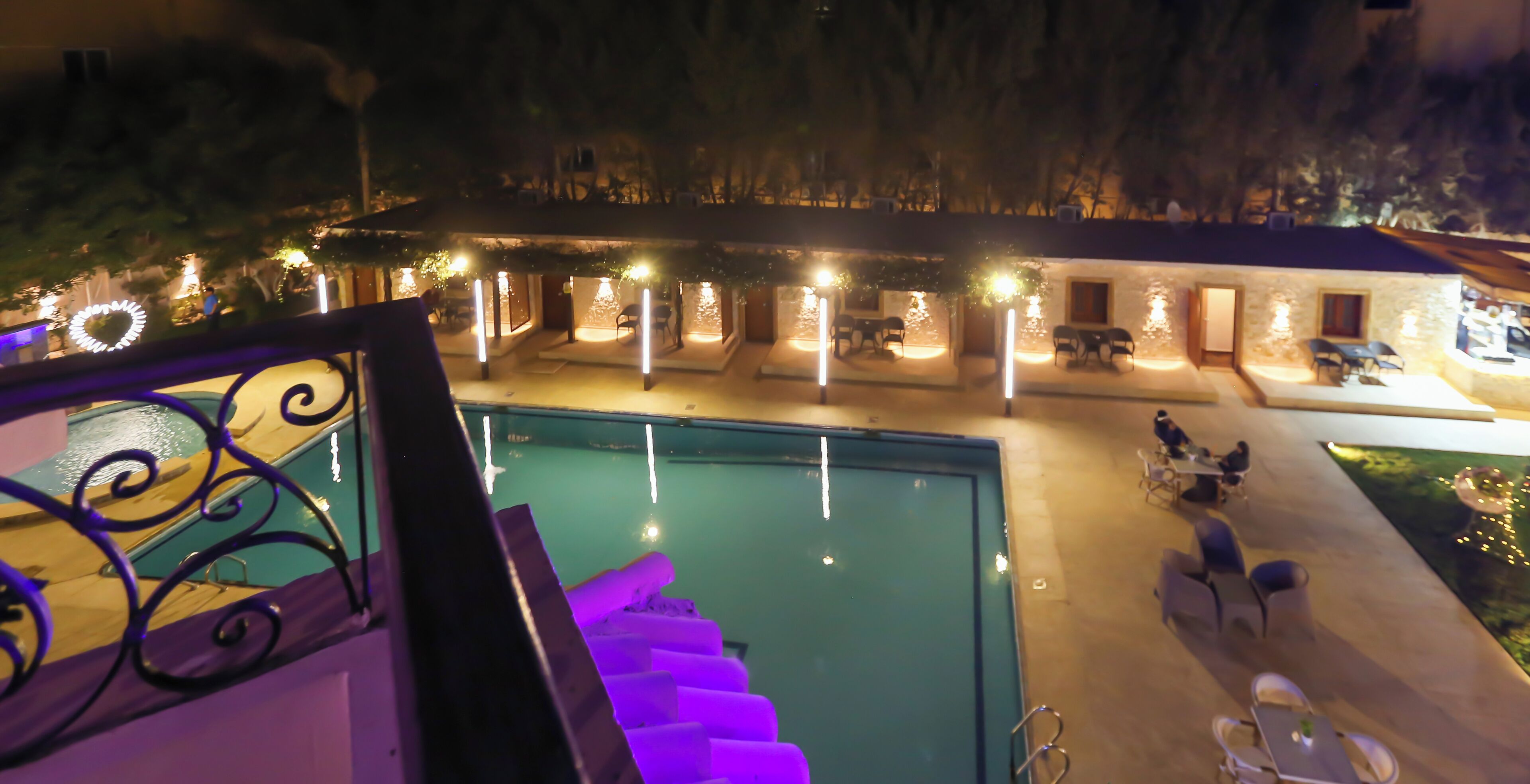 A pool area with a staircase leading down, surrounded by outdoor seating and illuminated by string lights.