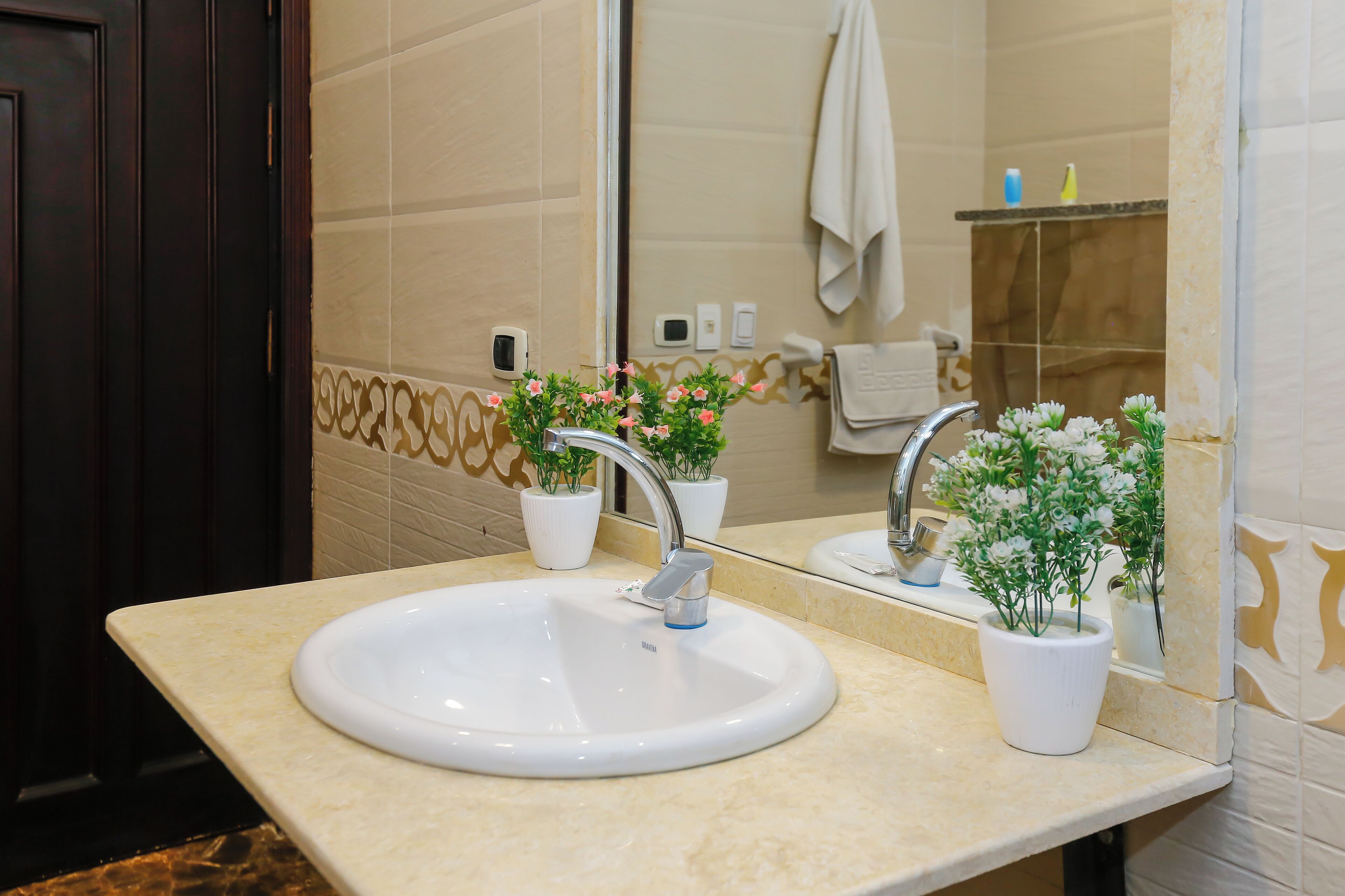 Un baño con un lavamanos blanco, dos espejos y dos plantas en macetas.
