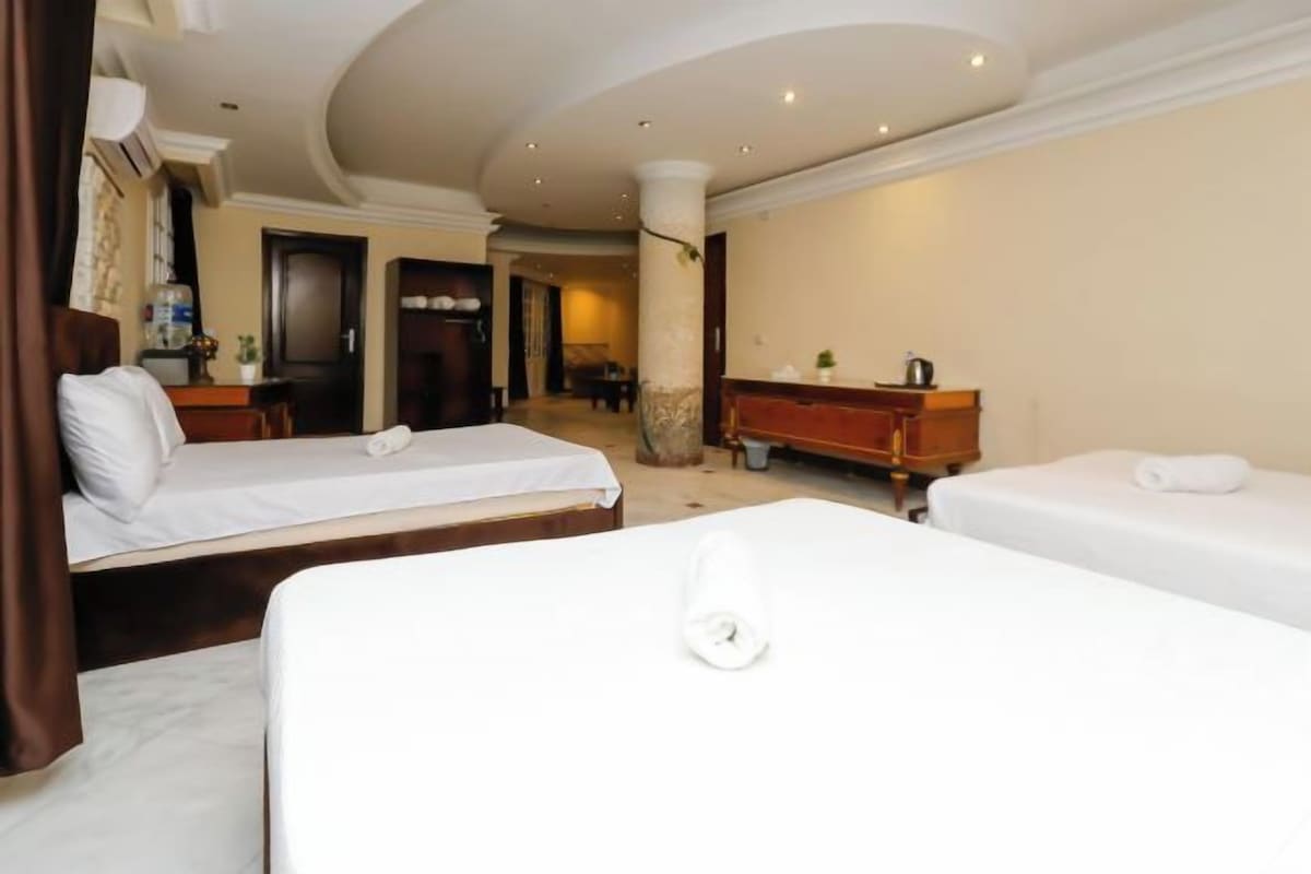 A hotel room with two beds, a wooden dresser, and a large pillar.
