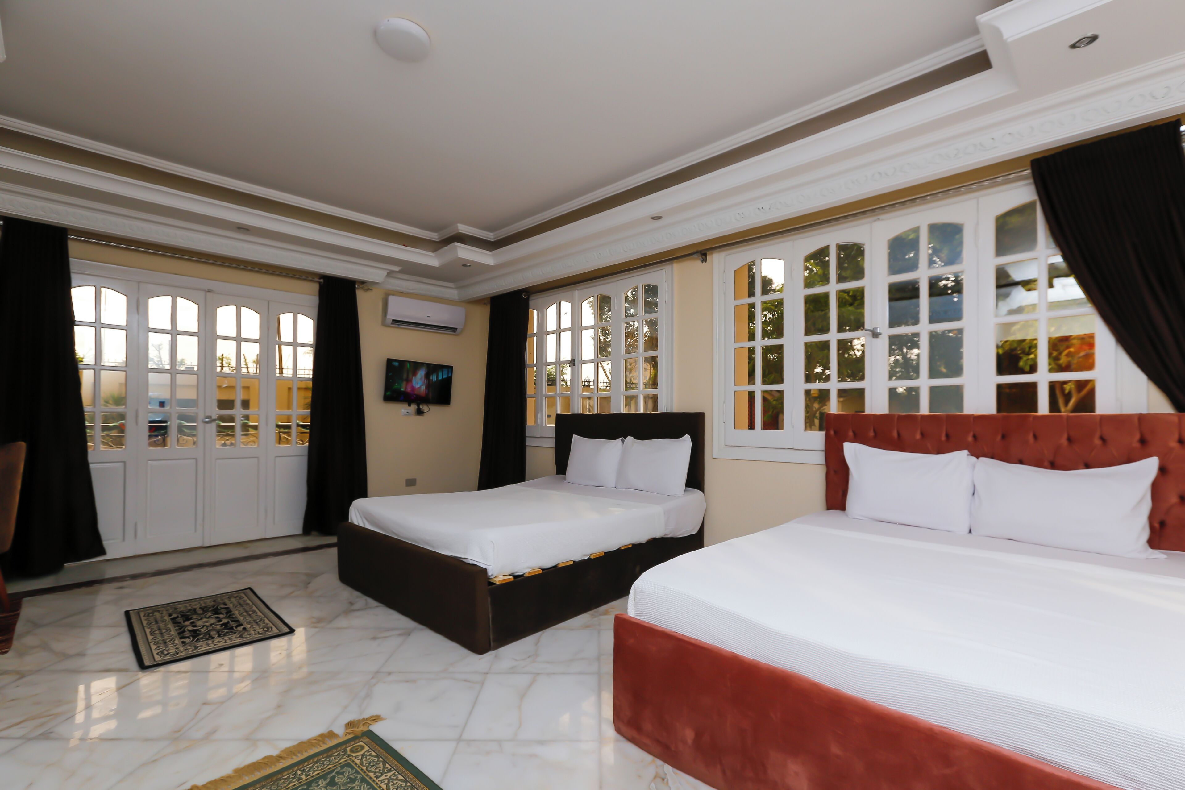 A hotel room with two beds, a marble floor, and large windows with curtains.