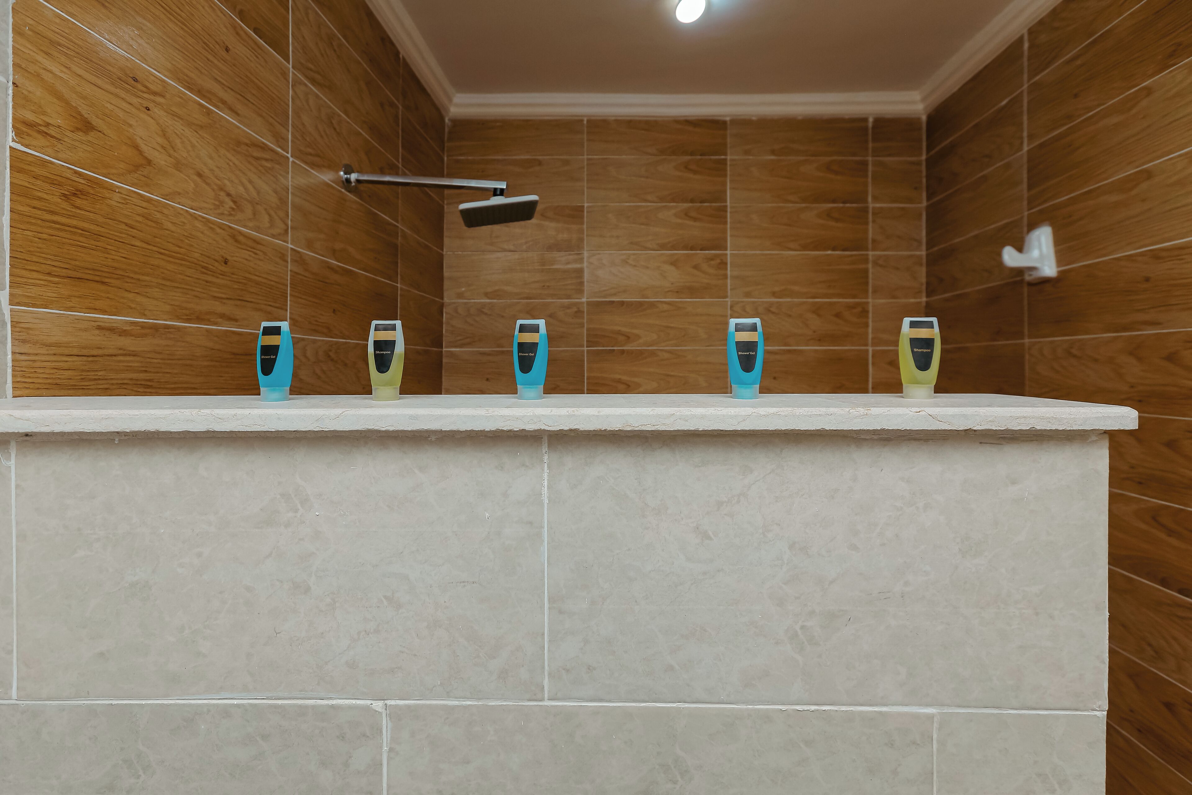 Een badkamer met houten wanden, een betegeld douchegedeelte en een wastafel met vier zeepdispensers.