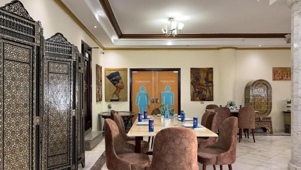 Een eethoek met een tafel voor vier personen, omringd door stoelen. Er zijn decoratieve panelen aan de muren en een kroonluchter boven de tafel.