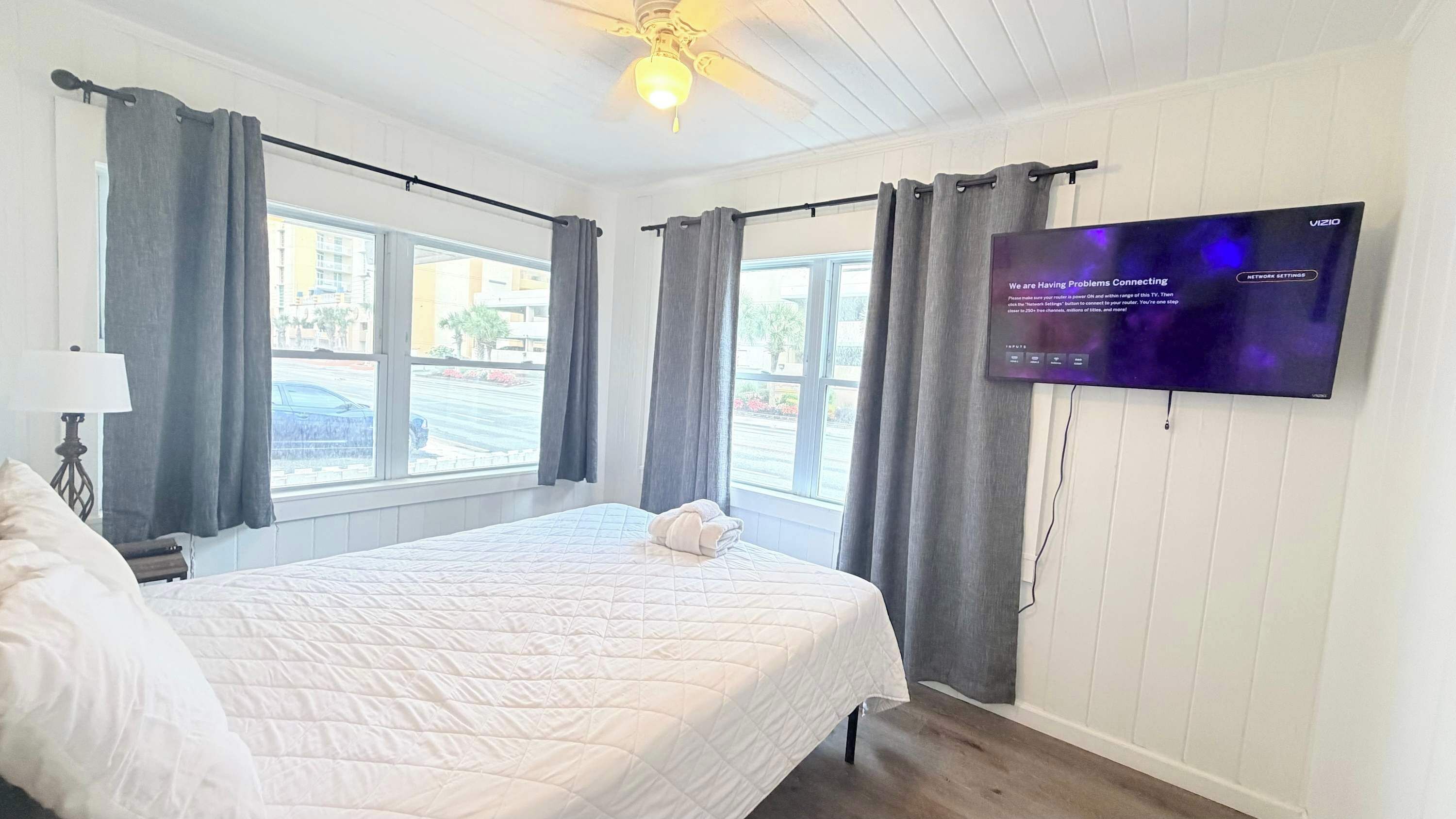 Hotellihuone, jossa on sänky, seinälle asennettu televisio ja ikkuna, jossa on verhot.