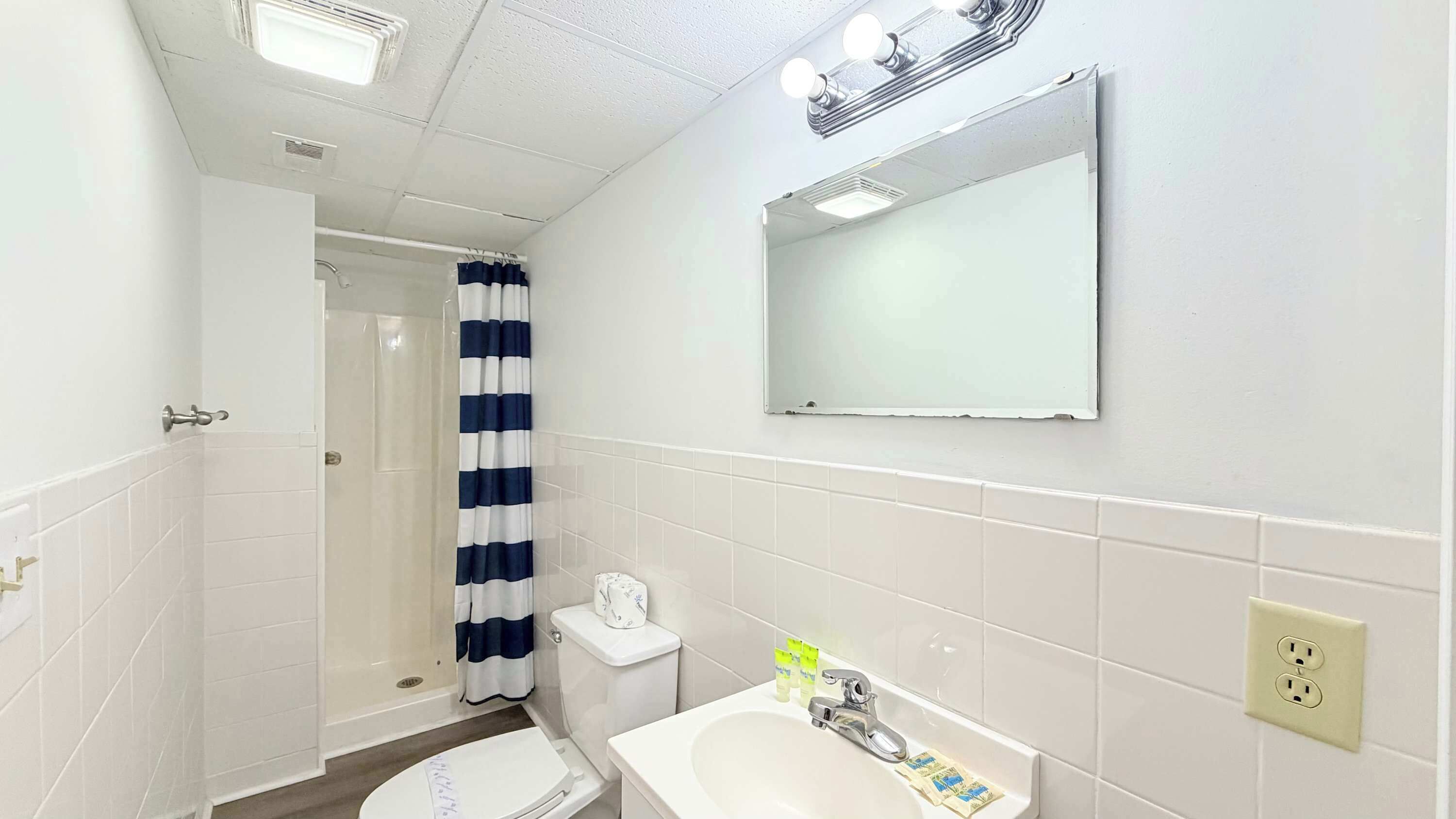 Un baño con ducha, inodoro, lavamanos y espejo.