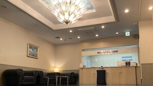 A hotel reception area with a modern chandelier, a reception desk, a seating area with sofas, and a framed picture on the wall. - HOTEL THE NEXT KANKU (Sennan)