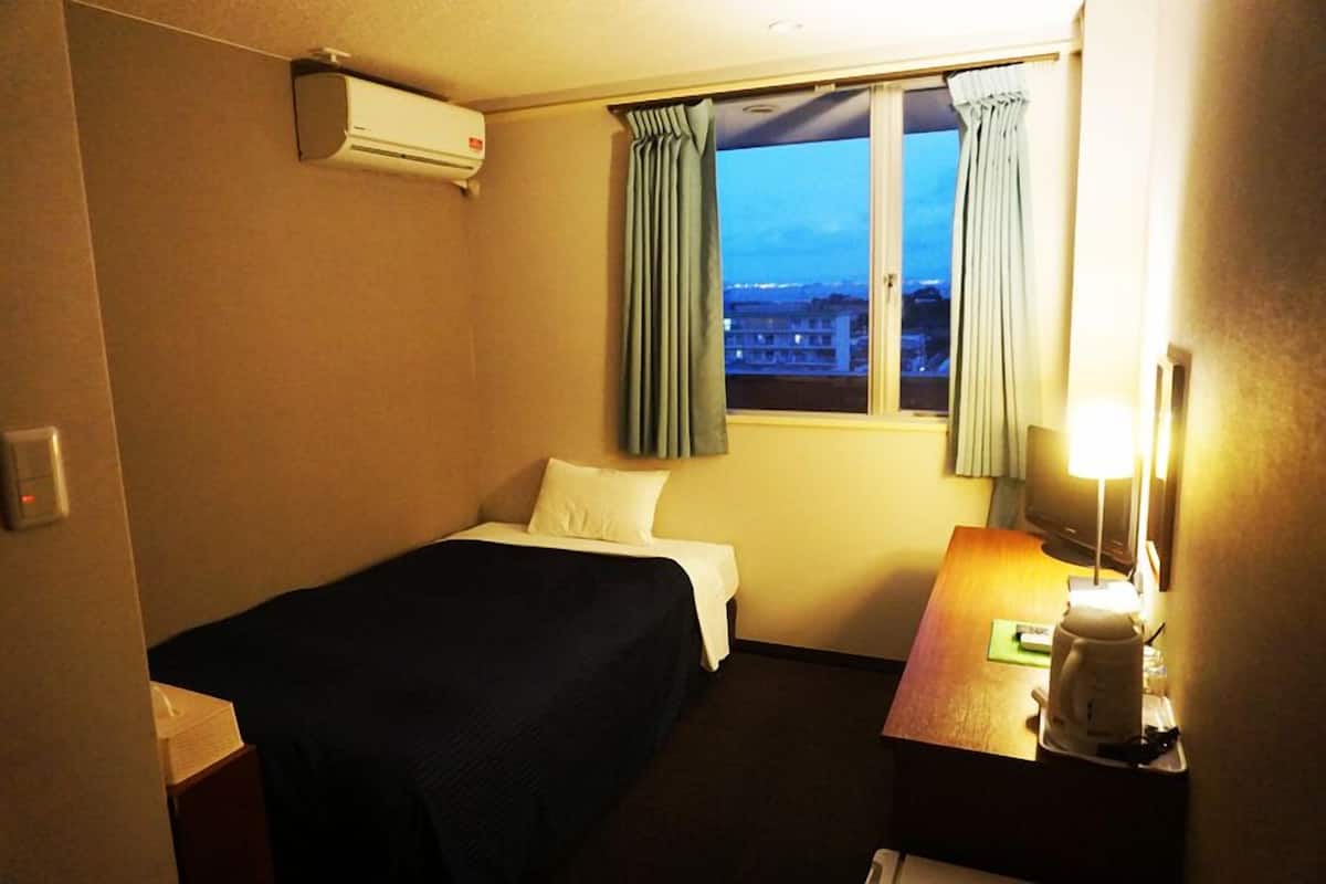 Une chambre d’hôtel comprenant un lit, un bureau avec une lampe, une fenêtre avec des rideaux et un appareil de climatisation.