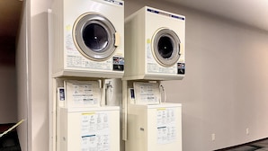Two stacked, white, front-loading washing machines in a room with a tiled floor and a plain wall. - HOTEL THE NEXT KANKU (Sennan)
