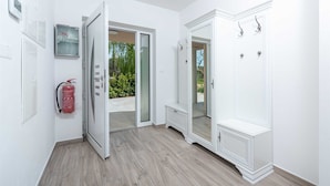 Ein Flur mit einem Feuerlöscher, einer Tür zum Ausgang und einem weißen Schrank mit Haken.