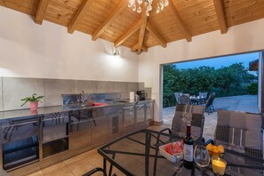 Een moderne keuken met een groot eiland, een eethoek met buitenmeubilair en uitzicht op groen.