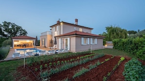 Ein zweistöckiges Haus mit Swimmingpool, Sitzgelegenheiten im Freien und einem Garten mit Pflanzenreihen.