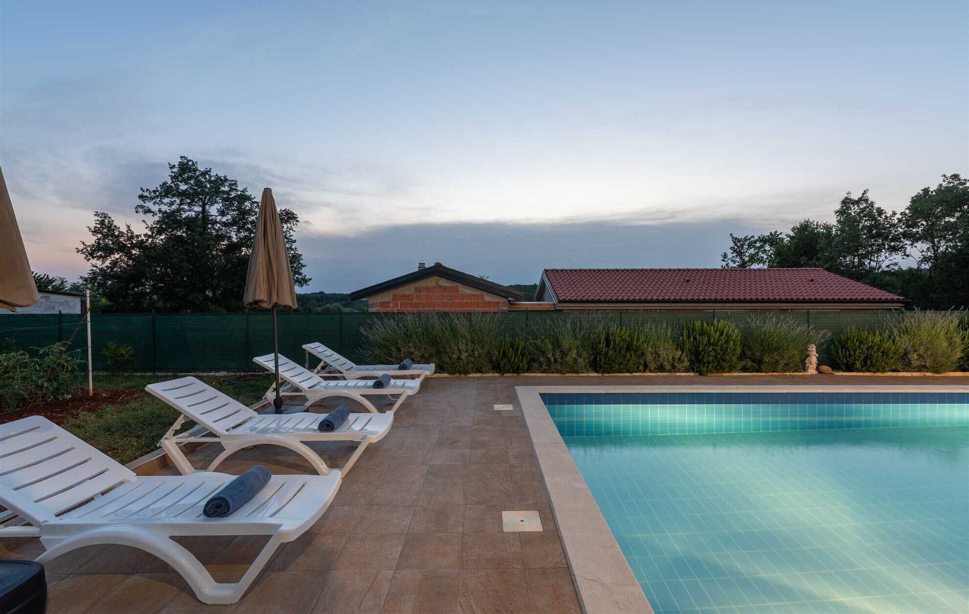 A pool area with lounge chairs and an umbrella, surrounded by a fence and vegetation.