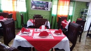 A restaurant with tables set with red napkins and white tablecloths, green walls, and a tiled floor. - Dilias house RANCH (Sabana Larga)