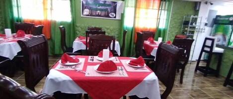 A restaurant with tables set with red napkins and white tablecloths, green walls, and a tiled floor.