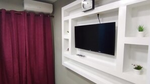 A room with a mounted TV on a white wall, a red curtain, and a small potted plant. - Dilias house RANCH (Sabana Larga)