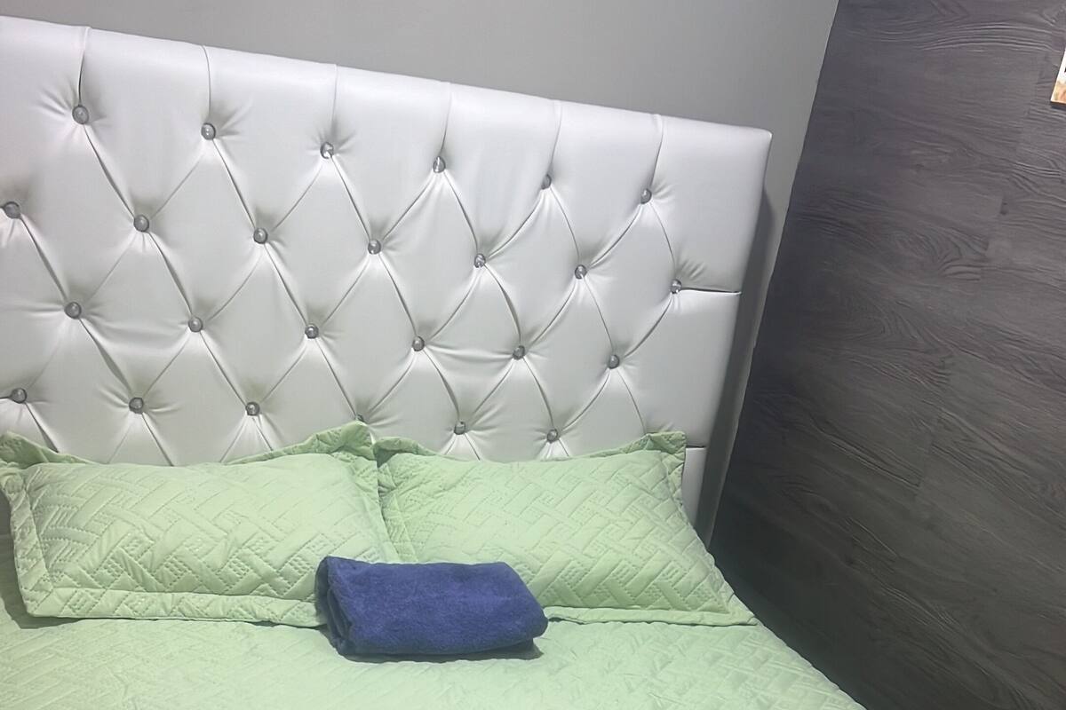 Una cama con cabecera capitonada, colcha verde y dos almohadas.