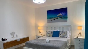 A modern bedroom with a bed, bedside tables, a nightstand, a wall-mounted artwork, and a built-in bench with storage. - Conchita de Mar (Punta Cana)