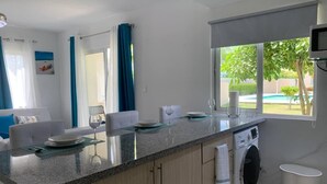 A compact kitchen with a washing machine, a dining area with a table and chairs, and a view of a swimming pool through large windows. - Conchita de Mar (Punta Cana)